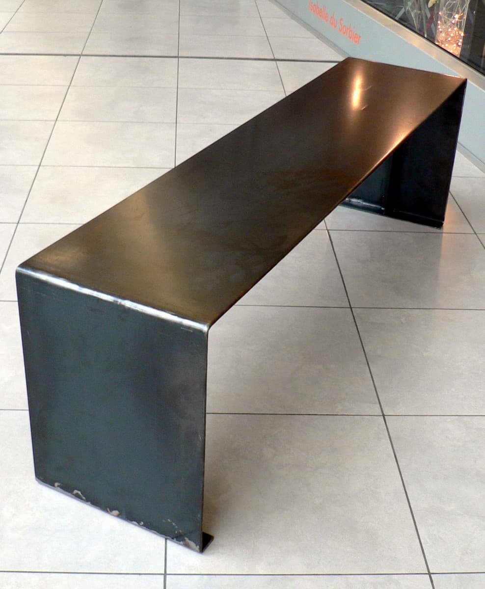 Banc contemporain au design minimaliste en acier plié mettant en valeur les reflets de la matière sur un sol clair. "ULTIMO"