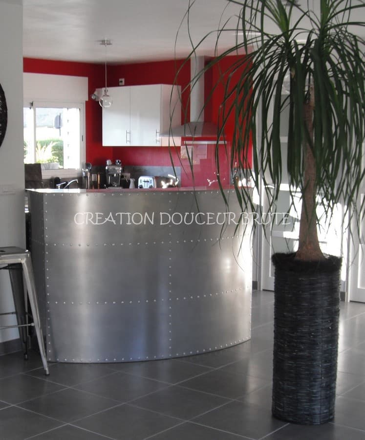 Comptoir de bar de cuisine arrondi en acier brossé avec rivets apparents, installé dans un intérieur contemporain.