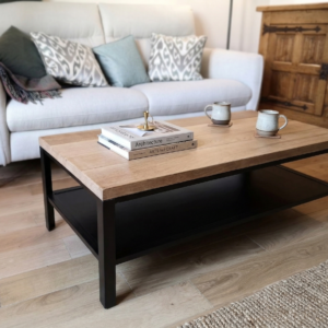Table basse industrielle en bois massif clair avec structure en métal noir, placée devant un canapé blanc dans un salon moderne.