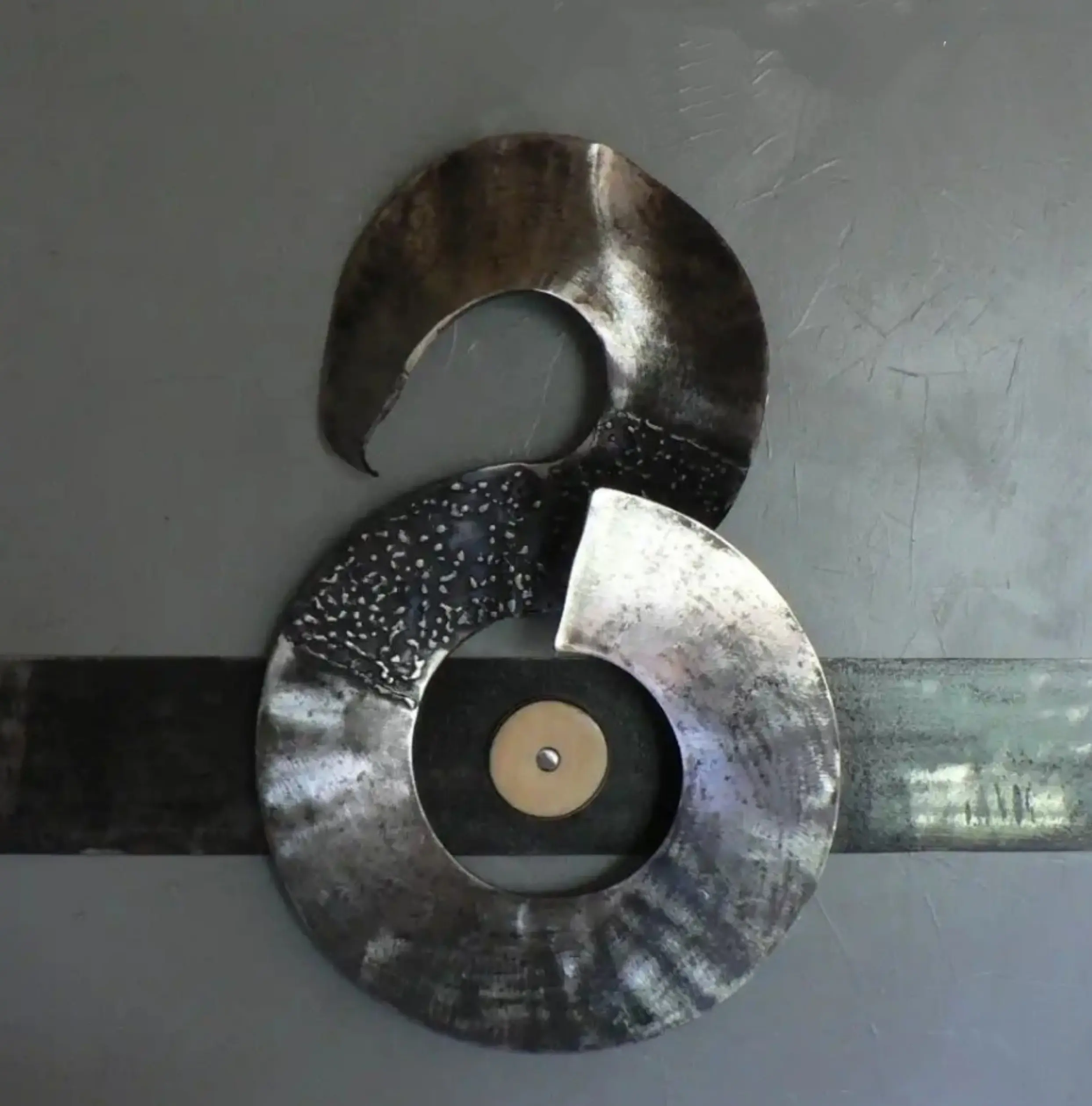 sculpture métallique contemporaine, forme circulaire en deux anneaux superposés avec patine gris métallique, fond neutre.