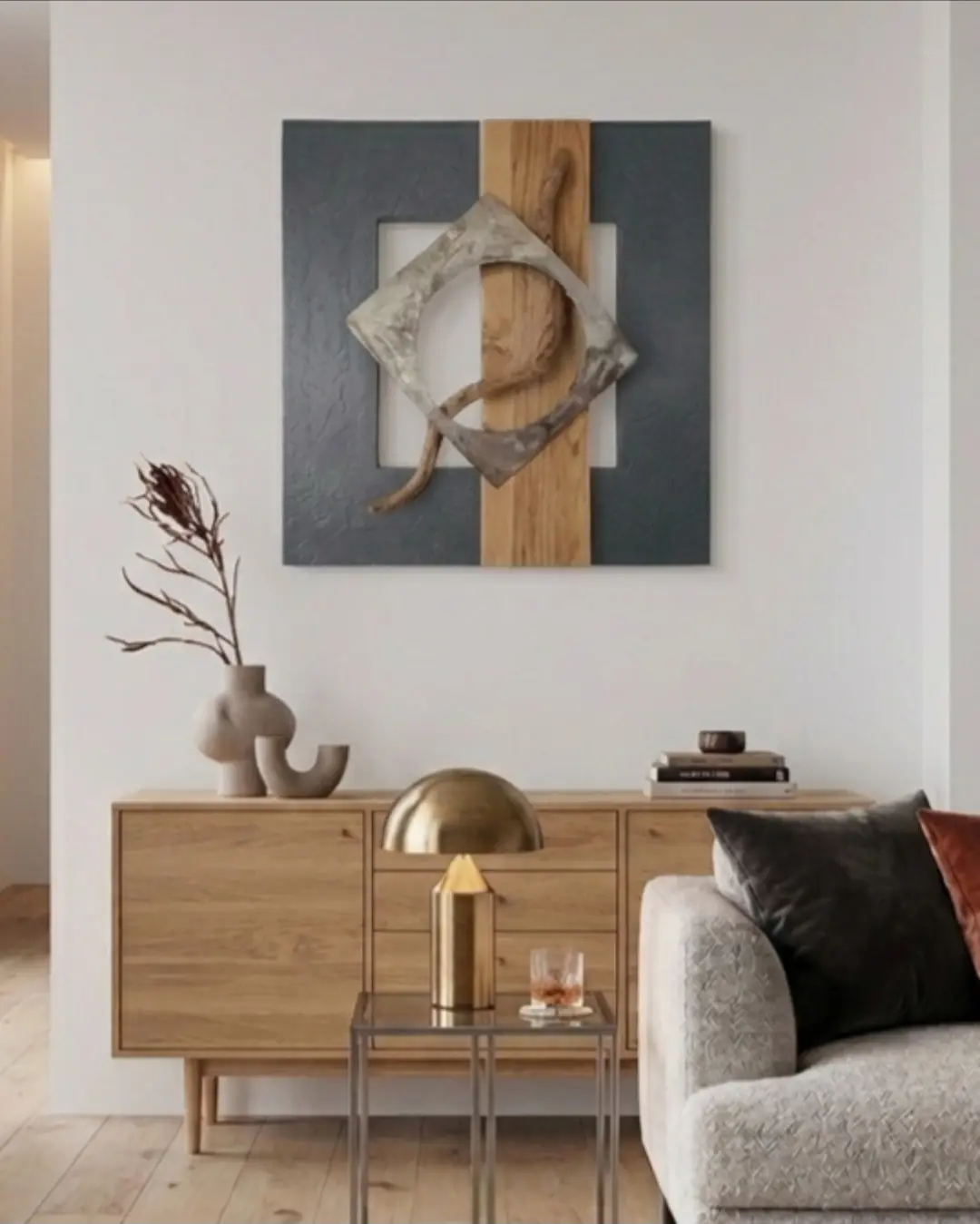 Tableau abstrait moderne sur fond blanc, encadré par une console bois massif et métal, avec vase décoratif et objets design sur la commode. Style éco-responsable et contemporain.